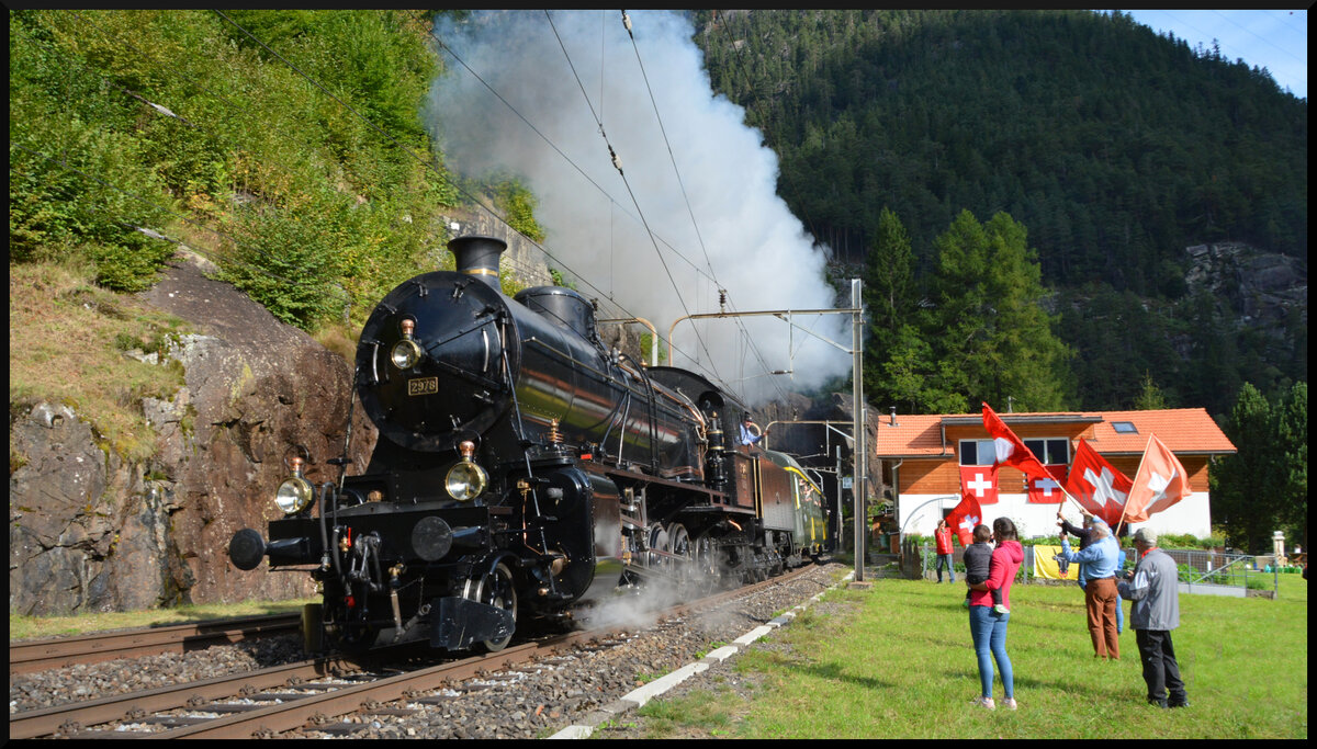 GOTTHARD-BAHNTAGE 2025: Der  Elefant  C 5/6 2978 (SBB Historic) stampft am 13.09.2025 mit Volldampf und dem Extrazug oberhalb von Wassen am Fahnenschwinger Xaver Andermatt und seinen Freunden vorbei die Gotthardnordrampe nach Göschenen hinauf.