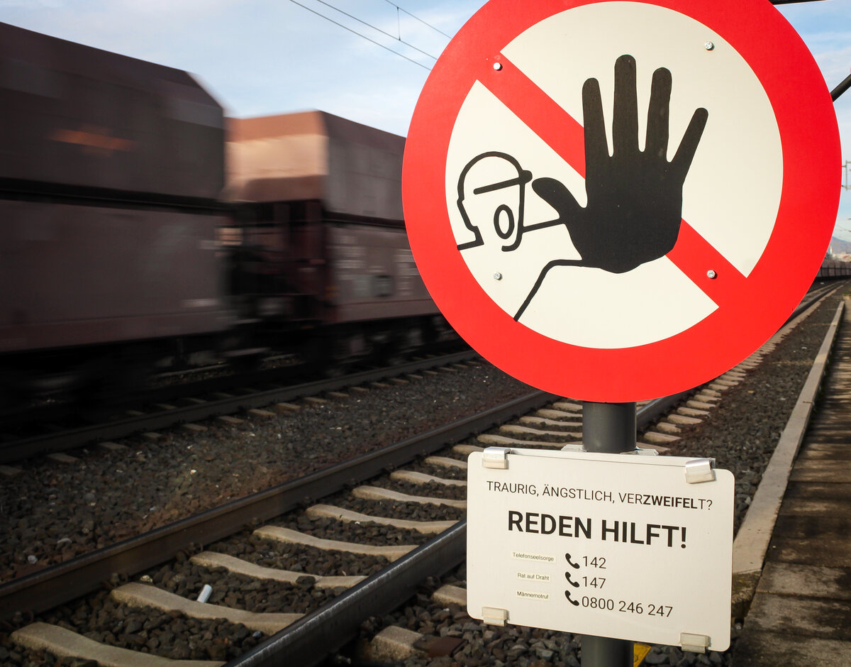Graz. Zur Suizidprävention wurden an zwei Bahnhöfen in Graz Schilder mit Notrufnummern aufgestellt. Im Hintergrund rauscht ein Güterzug aus Slowenien vorbei; Graz Don Bosco, 11.11.2022