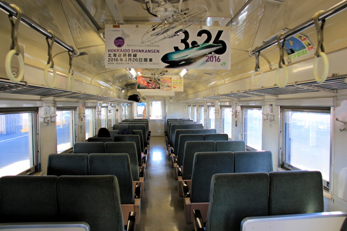 Hanasaki-Linie. Blick in den Triebwagen KIHA 54 523. An der Decke hängt die freudvolle Ankündigung, dass der Shinkansen im kommenden März den Betrieb bis auf Japans Nordinsel Hokkaidô aufnimmt. 26.Oktober 2015. 