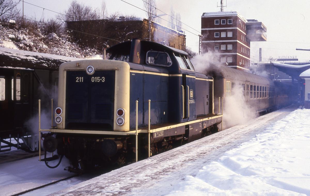 Harter Winterdienst am 13.1.1987 für 211015 im Hauptbahnhof Osnabrück. Auf Gleis 14 im unteren Bahnhof steht der Nahverkehrszug nach Bramsche bereit.