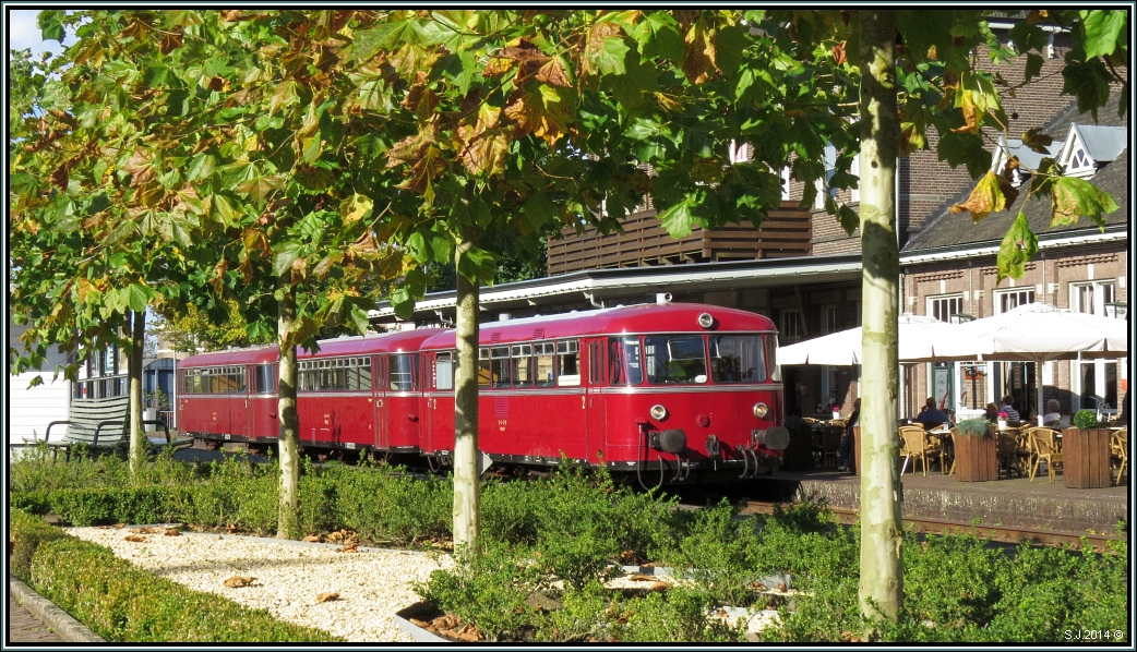 Herbststimmung am Bahnhof von Simpelveld in den Niederlanden. Die Blätter der Bäume zeigen ihre Brauntöne,die Sonne erwärmt das Szenario angenehm stimmig,und die Leute verweilen noch draussen und geniessen ihren Kaffee und das ein oder andere Bierchen.
Derweil wartet der Schienenbus auf Fahrgäste. Nostalgie bei der ZLSM im Oktober 2014.