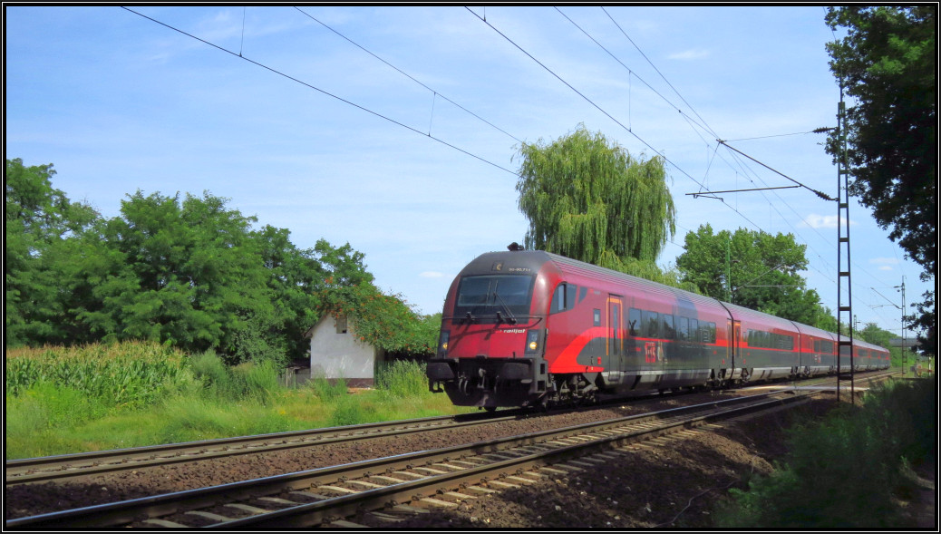 Hier ist der Railjet aus Budapest auf freier Strecke zu sehen. Er passiert gerade den Bahnübergang zwischen Komárom und Ács auf der ungarischen Kbs 1.Szenario vom 01.August 2015.