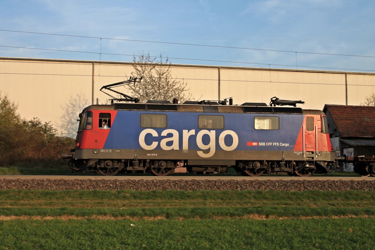 Hier eine Seitenansicht vom 29.03.2014 von der SBB Cargo Re 421 374-0, als sie mit einem langem gemischten Containerzug durch den kleinen Ort Auggen, an der KBS 703 gelegen, gen Freiburg fuhr und von der Abendsonne angestrahlt wurde.