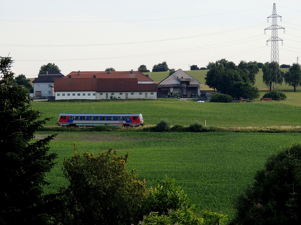 Hinter den Bäumen, und zwischen den Feldern; tuckert ein Triebwagen der BR5047 als R3492 auf der Hausruckbahn in Richtung Attnang; 150703