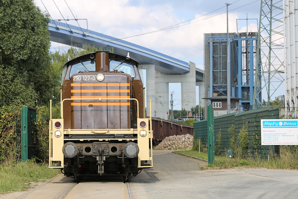 HSL Rangierlok 290 127 mit Kies-Wagen im Anschluß Stralsund Südhafen. Im Hintergrund ist die geöffnete Eisenbahn-u. Strassenklappbrücke über den Strelasund, sowie die Rügenbrücke zu sehen . - 05.09.2018