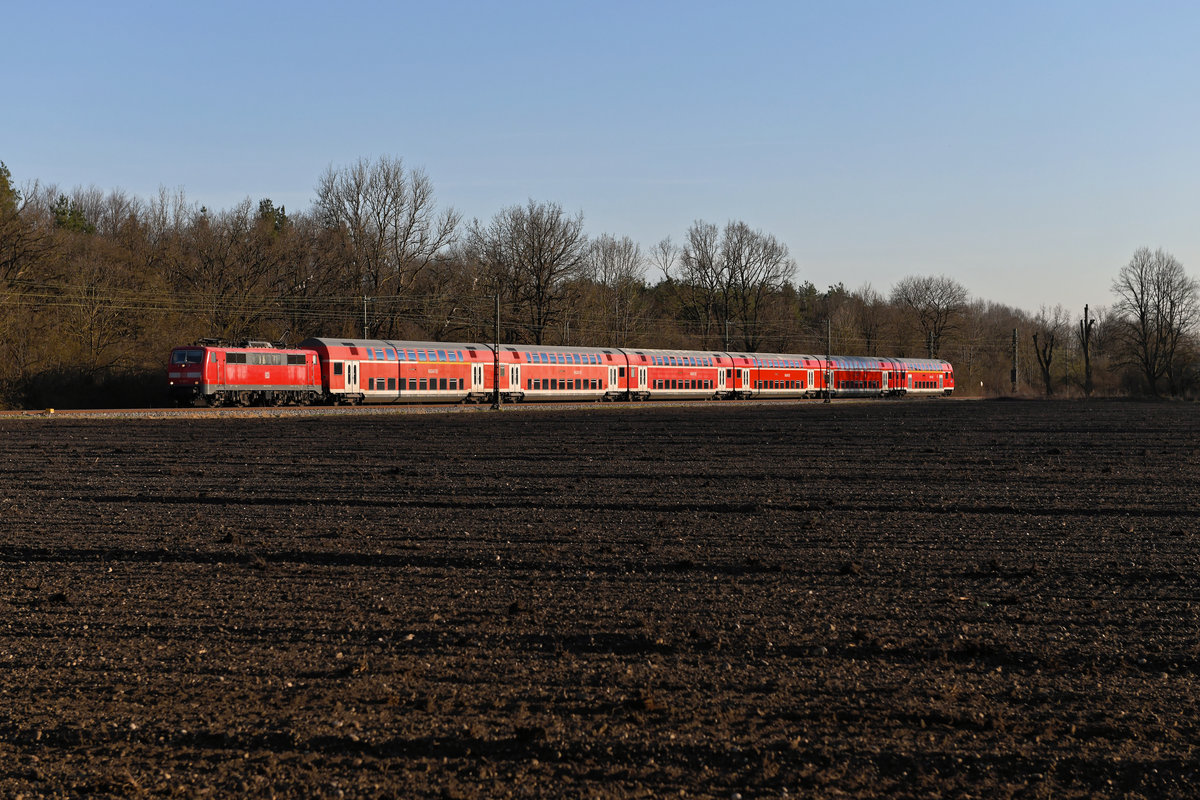 Im abendlichen Streiflicht konnte ich am 16. März 2020 die 111 187 mit ihrer RB 4862 nach Regensburg aufnehmen. Bei Obschleissheim eilte der Berufsverkehr-Verstärker am Korbianiholz vorbei. Die Doppelstockwagen aus der Serie 1993 sind inzwischen mit das älteste Wagenmaterial bei DB Regio und haben keine große Zukunft mehr vor sich. 