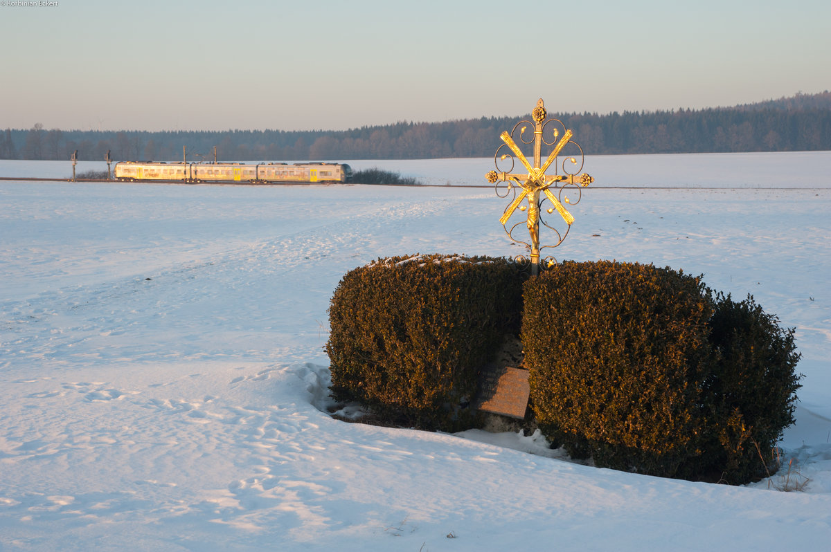 Im Abendlicht kurz vor Sonnenuntergang passte das Motiv bestens: Agilis Triebwagen 440 412 als ag 84203 von Neumarkt (Oberpf) nach Plattling passiert ein Wegkreuz am Straßenrand bei Seubersdorf, 21.01.2017 