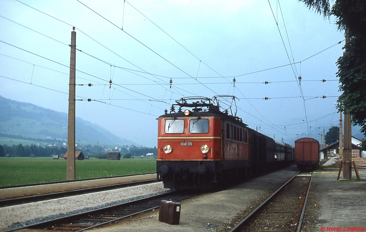 Im August 1980 fährt 1041.05 mit einem Regionalzug im Bahnhof Haus im Ennstal ein. Ohne ÖBB-Emblem wirkt die Lok etwas  nackt . Der Koffer im Vordergrund wurde als Stückgut im Gepäckwagen verstaut.