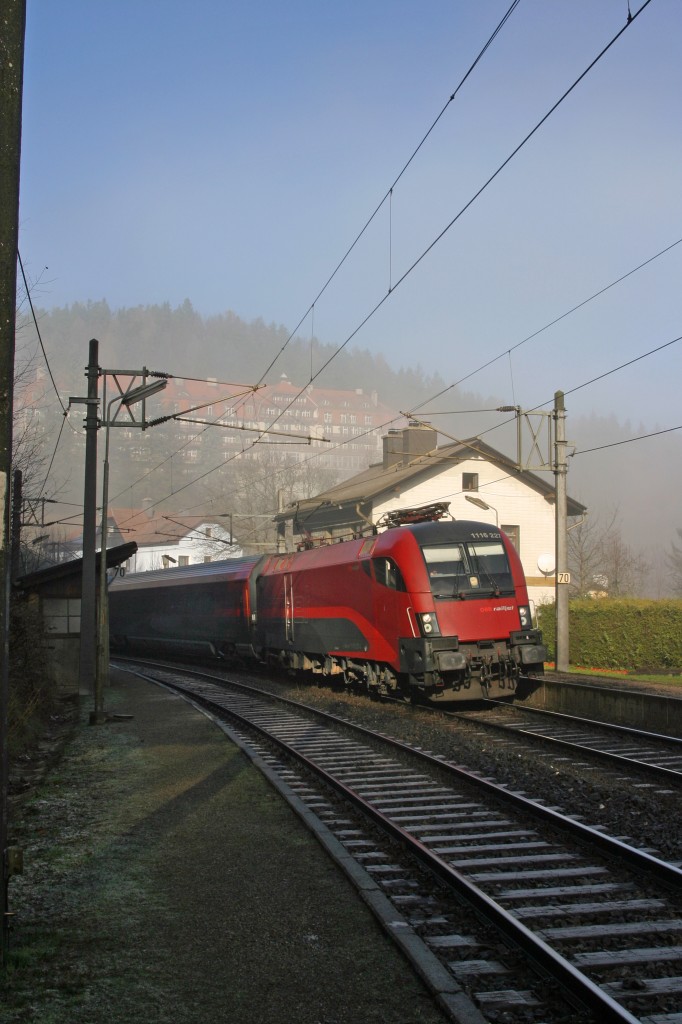 Im einzigen Sonnenfenster durchfährt RJ-15555 mit 1116.227 mit dem leicht Nebelverhangenen Kurhaus die Hst.Wolfsbergkogel am 23.11.14