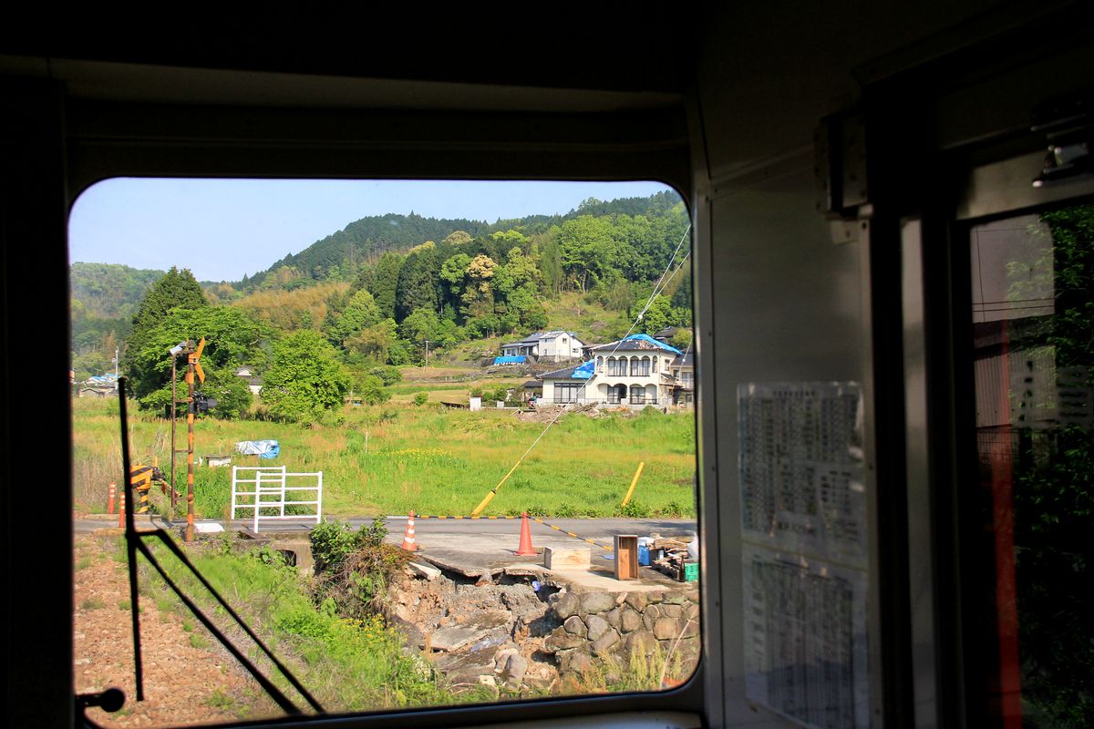 Im Erdbebengebiet von Zentral-Kyûshû: Ueberall sind die Schäden sichtbar, Schutt lagert sich vor den Häusern, im Vordergrund ist ein Stück Boden weggebrochen. Aus dem Dieseltriebwagen zwischen Tenjinyama und Shônai im Aufstieg in die Berge von Zentral-Kyûshû, 2.Mai 2016. KYÛDAI-HAUPTLINIE 