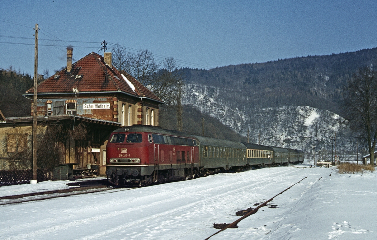 Im Februar 1978 durchfährt die Kasseler 216 212 mit E 2833, dem Nachfolger des legendären  Heckeneilzugs  Bremen-Frankfurt, den Bahnhof Schmittlotheim im Edertal. E 2833 startete in Hamburg und fuhr über Neben- und untergeordnete Hauptbahnen, u.a. der elektrifizierten  Natobahn  Nienburg-Minden und Herford-Altenbeken-Warburg nach Brilon-Wald und ab dort auf seinem angestammten Laufweg nach Frankfurt.   