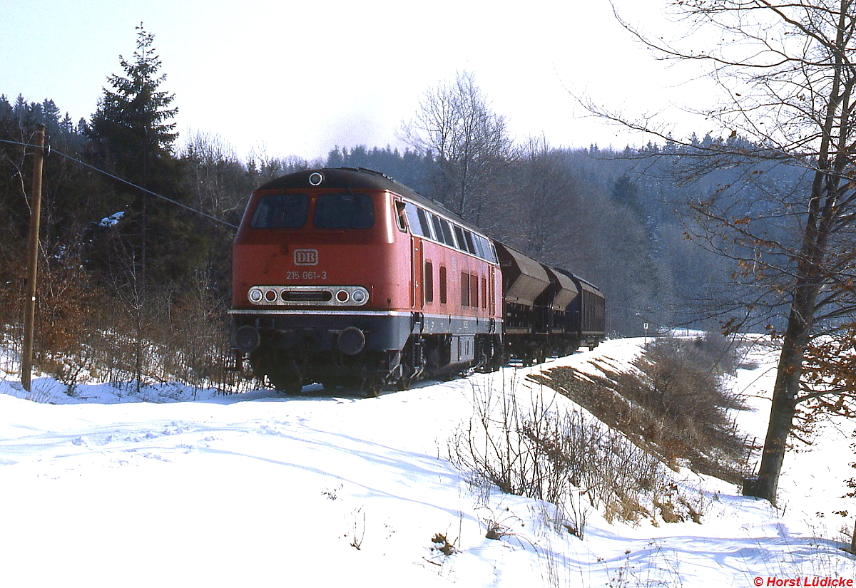 Im Februar 1983 ist 215 061-3 auf der Roßberger Steige nach Bad Wurzach unterwegs. Damals war die Strecke nur noch wegen des Güterverkehrs von und zur Glashütte in Bad Wurzach in Betrieb. 2004 erwarb die Stadt Bad Wurzach die Strecke, heute findet an Sonntagen gelegentlich auch Personenverkehr statt.