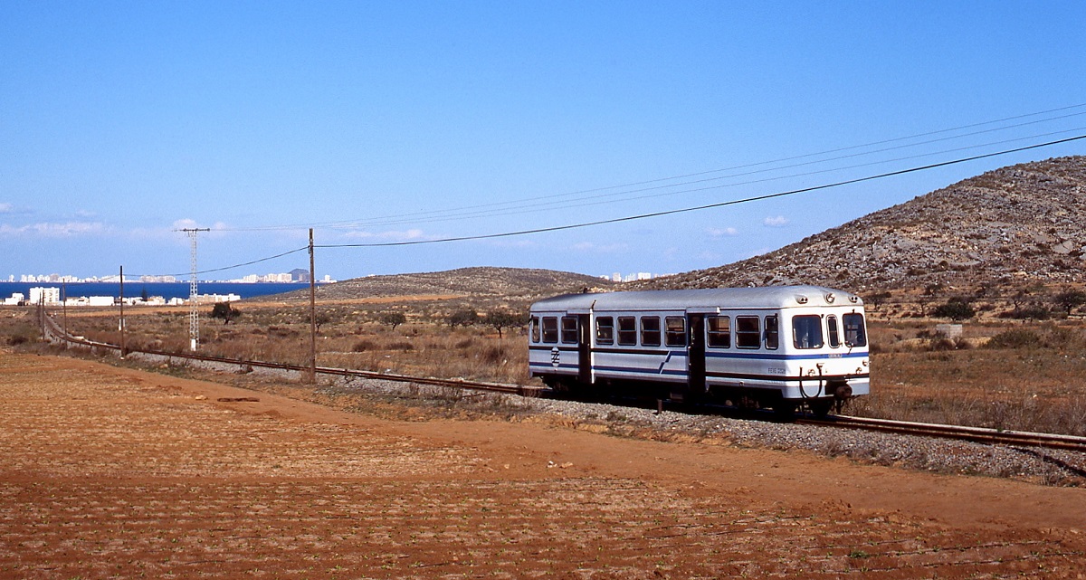 Im Februar 1996 hat ein FEVE-Triebwagen der Reihe 2300 Los Nietos verlassen und sich auf den Weg nach Cartagena gemacht, im Hintergrund die Bettenburgen von Los Nietos