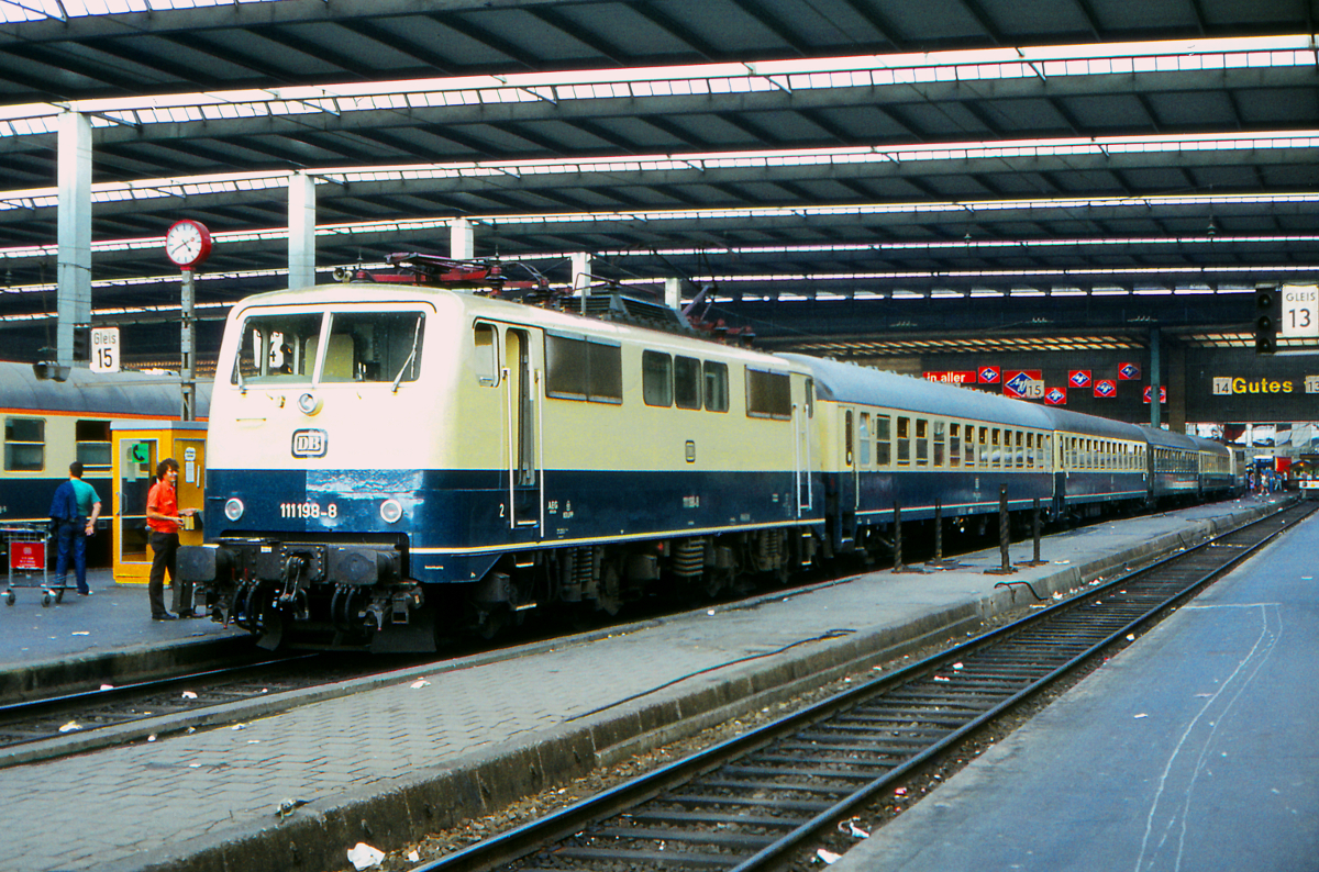 Im Jahr 1983 wurde die vorletzte Serie der Baureihe 111 fabrikneu an das Bw München 1 abgeliefert. Der saubere, strahlende Lack war jedes Mal ein besonderer Eindruck. Die 111 198 ist noch nicht lange im Dienst, als ich sie am 20. August 1983, einem Samstag, fotografieren konnte. Der Zug ist der zweite Teil des D284 aus Meran nach Frankfurt am Main über Stuttgart. Neubaustrecken und ICE waren damals noch in weiter Ferne, aber in den Abteilwagen ließen sich die vielen Stunden einer Reise mit der Eisenbahn bequem verbringen. August 1983.
Canon AE1, Canoscan, GIMP 