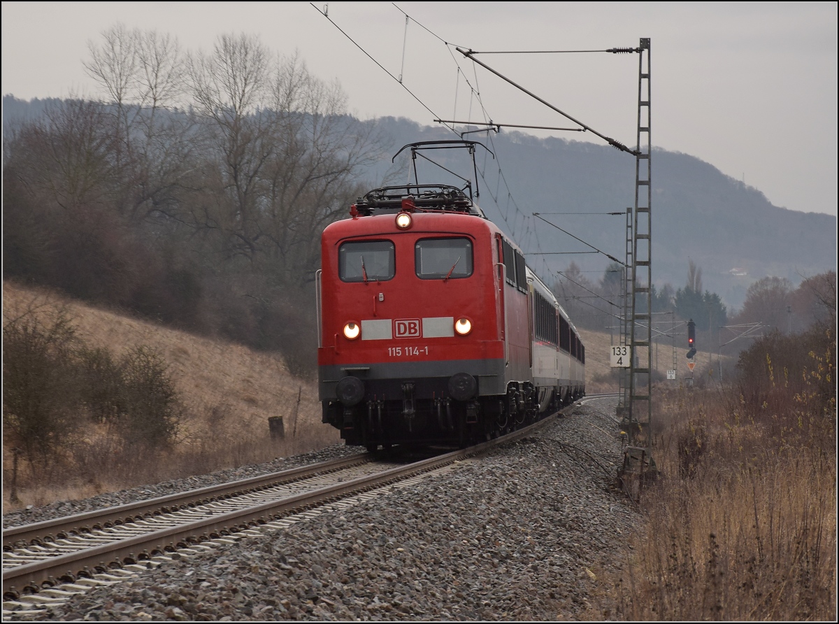 Im nunmehr 67. Jahr der Karriere dieser Baureihe ist die mittlerweile 59-jährige 115 114-1 noch immer zeitweise im hochwertigen Planverkehr beschäftigt und bringt einen IC von Singen nach Stuttgart. Im Hintergrund der knapp 1000 m hohe Dreifaltigkeitsberg. Aldingen, Dezember 2016.
