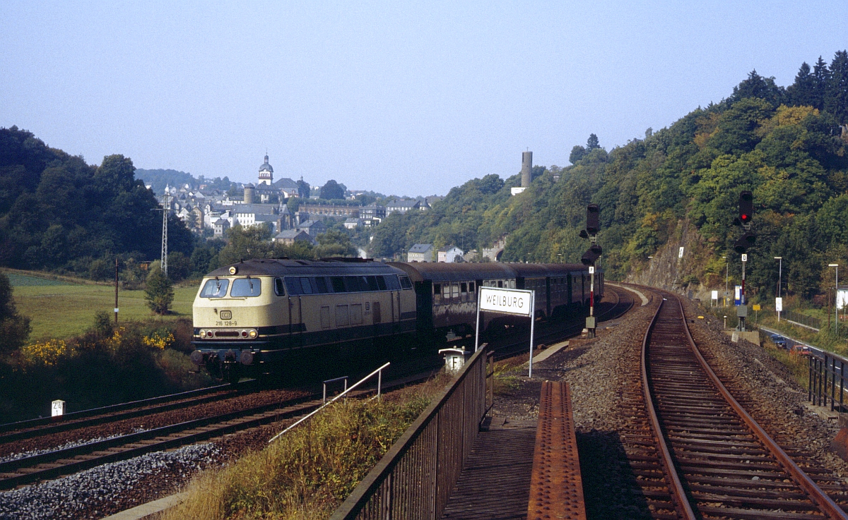 Im Oktober 1984 lagen in Weilburg noch die Gleise in Richtung Weilmünster, wurden aber nur noch sporadisch befahren. 216 128 ist mit ihren aus Umbau-Vierachsern bestehenden Eilzug nach Koblenz unterwegs. 