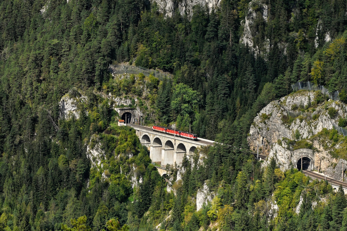 Im Rahmen einer Wanderung wurde auch der sogenannte  20-Schilling-Blick  umgesetzt. Bei Wolfsbergkogel hat man von einem Aussichtsturm einen guten Überblick über diverse interessante Bauwerke der Semmeringbahn. Die inzwischen zum Weltkulturerbe der UNESCO erklärte Gebirgsbahn hat eine große Bedeutung für Österreich. Einst wurde sie auch als Motiv auf einem Geldschein gewürdigt. Die Kalte Rinne war auf der Rückseite der vorletzten Ausgabe der 20-Schilling-Banknote zu sehen, die Vorderseite zeigte ein Porträt des Erbauers, Carl Ritter von Ghega. Auf dem Foto sieht man einen Lokzug talwärts in Richtung Payerbach-Reichenau fahren. Die drei 1144 hatten zuvor bei Güterzügen Vorspann- und Schubdienste geleistet und werden nun für neue Leistungen benötigt. Gerade haben sie den Tunnel durch die Polleroswand verlassen und befinden sich nun auf dem Krauselklause-Viadukt. Gleich wird es durch den kurzen Krausel-Tunnel gehen und bald wird der Bahnhof Breitenstein durchfahren (24. September 2020).