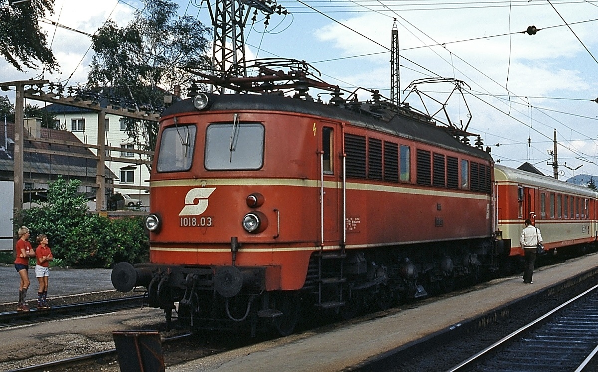 Im September 1986 wartet 1018.03 im September 1980 vor dem  Ausseerland  im Bahnhof Stainach-Irdning auf die Abfahrt nach Wien. Ob aus den beiden jugendlichen  Lokspähern  später einmal Eisenbahnfans geworden sind?