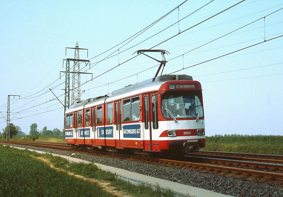 Im Sommer 1980 ist der Rheinbahn-GT8S 3052 zwischen Duisburg-Kesselsberg und Düsseldorf-Froschenteich unterwegs. Nach Gründung des Verkehrsverbundes Rhein-Ruhr wurde die ehemalige Linie D in 79 umgezeichnet, heute verkehrt sie als U 79. Der 3052 zeigt sich noch in der Ursprungsausführung, erst mit der Eröffnung des ersten U-Bahn-Tunnels in Düsseldorf 1981 wurden 36 GT8S zu GT8SU für den Einsatz an Hochbahnsteigen umgebaut.