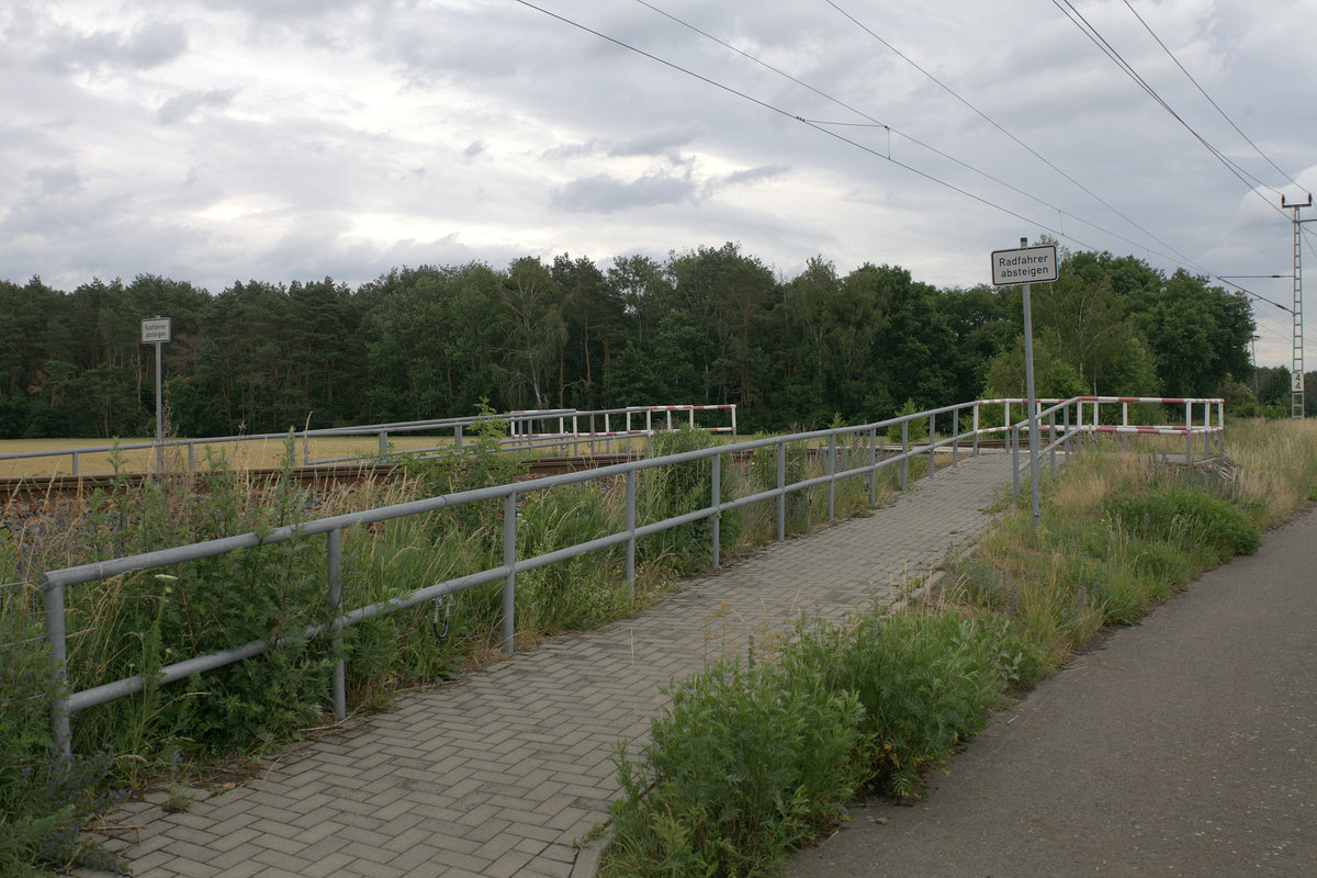 Im südöstlichen Landesteil von Brandenburg gibt es ein verbreitetes Radwegnetz, teilweise gut ausgebaut. In der Nähe von Ruhland ist ein extra Wegeübergang angelegt worden, durch Geländer gesichert, so dass man als Radfahrer absteigen muss, allerdings fehlen die Warnkreuze, nur ein Schild  Radfahrer absteigen  ist aufgestellt. Beim Überqueren lässt sich natürlich, im Gleis, auf dem BÜ stehend, ein Bild von der Strecke schießen.20.06.2020 12:37 Uhr. Radtour.
Die Geoposition weist diesen real existierenden BÜ leider nicht als BÜ aus.
Strecke Hosena-Senftenberg.