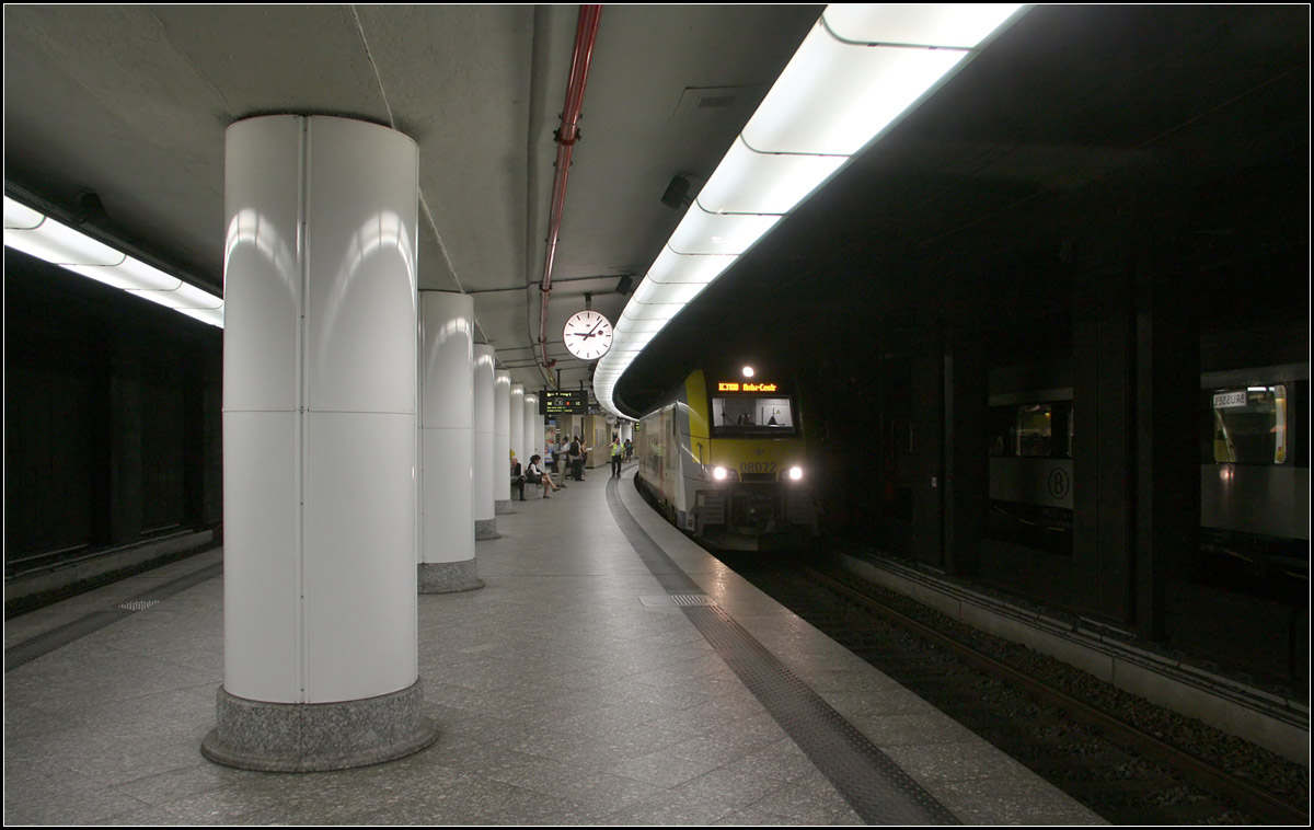 Im Tunnel durch Brüssel -

Blick in die unterirdisch liegenden Bahnsteige des Brüssler Zentralbahnhofes. Der Bahnhof, wie auch die gesamte Tunnelstrecke zwischen Brüssel Noord und Brüssel Midi hat sechs Gleise. Die Hochgeschwindigkeitszüge fahren auch durch den Tunnel, halten hier aber nicht.

Der Bau der Tunnelstrecke wurde 1911 begonnen und wurde erst 1952 fertiggestellt. Neben Bruxelles-Central gibt es noch die unterirdische Station Bruxelles-Congrès/-Congres und im Süden schon außerhalb des Tunnels gelegen die Station Bruxelles-Chapelle/Kapellekerk. Der Tunnel führt recht kurvenreich entlang des Hanges zwischen der Ober- und Unterstadt durch Brüssel. Auch die Bahnsteige in Bruxelles-Central liegen im Bogen.

23.06.2016 (M)

