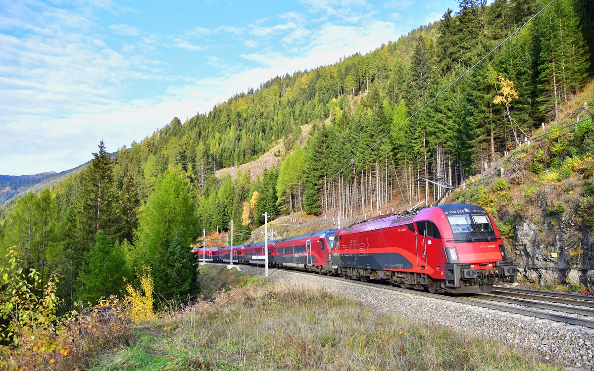 Im warmen Spätnachmittagslicht des 26.10.2026 war 1216 020 mit dem RJ 87 nach Bologna Centrale in den herbstlichen Wäldern bei Gries am Brenner unterwegs.