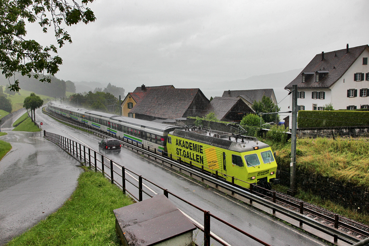 In Bollingen bekommt der Voralpenexpress eine kräftigen 
Platzregen aufs Dach als die Re 446 018  Akademie St.Gallen  zusammen mit der Schublok Re 446 017 von Schmerikon nach Rapperswil unterwegs ist.Bild 14.7.2016
