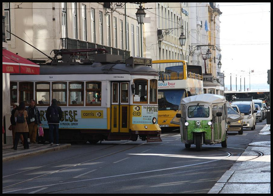 In den engen Straßen der Lissaboner Altstadt müssen, wie hier nahe dem Terreiro do Paco, die Tram Bahn Wagen über die Gegenfahrbahn einbiegen, um in andere Straßen zu gelangen. Hier wartet eine Tram beim Abbiegen am 21.3.2018 zunächst die Durchfahrt eines TucTuc ab.