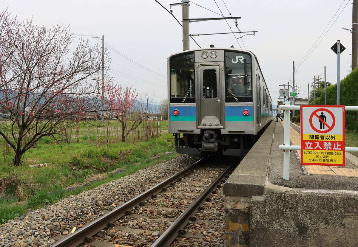 In den japanischen Alpen - Zug E 127-111 hält in Azumi Kutsukake. Die Bahnsteighöhe in Japan entspricht grundsätzlich dem Wagenboden des Zuges. Aufnahme von einem Bahnübergang aus. 21.April 2022 