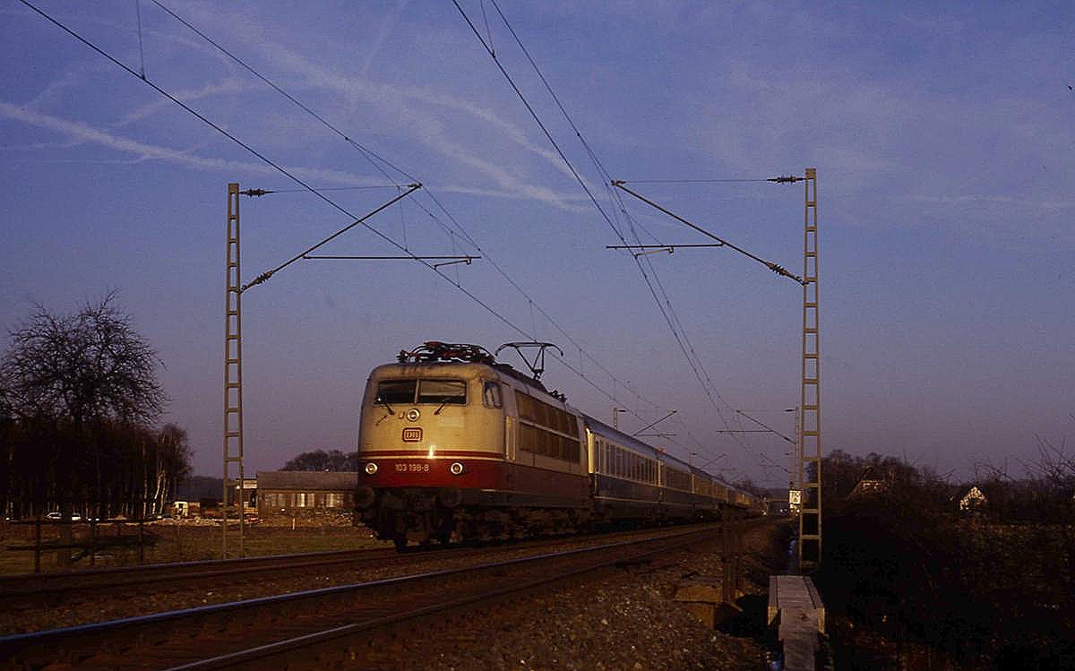 In der letzten Abendsonne fährt 103198 mit dem EC 30  Merkur  auf der Rollbahn Richtung Ruhrgebiet am 25.2.1987 um 16.43 Uhr in Hasbergen Höhe Wilkenbach vorbei.