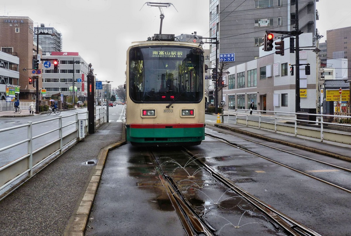 In Toyama am Japanischen Meer fegen eisige Blizzards etwa alle halbe Stunde ber die Stadt. Oft gefriert der Schnee am Boden dann zu Eis. So haben fast alle Strassen, und ebenso alle Strassenbahnweichen Sprinkleranlagen. Das Wasser, das wrmer ist als die Luft, hilft Eisbildung zu verhindern. Im Bild steht Wagen 8003 der Strassenbahn Toyama beim Bahnhof, bereit zum Gleis- und Richtungswechsel. 2.Mrz 2013. 