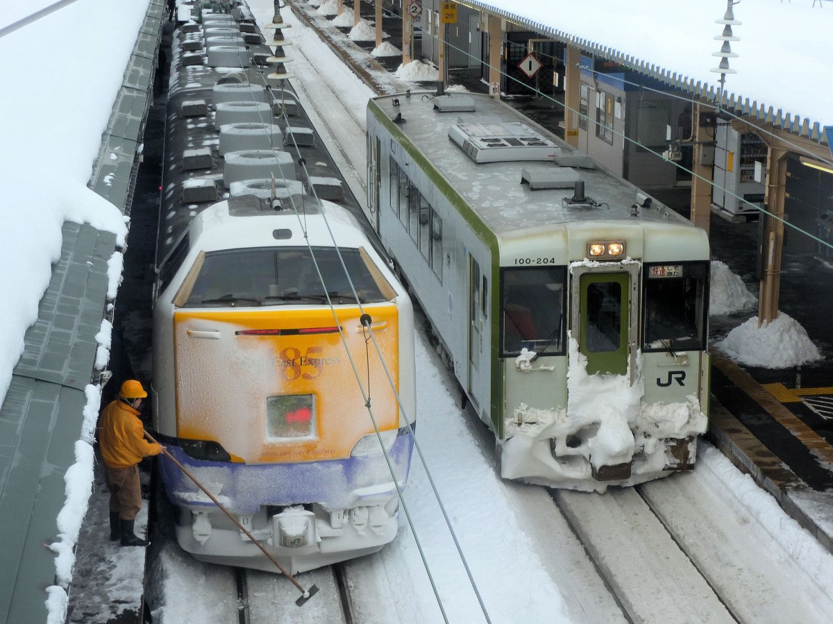 Intercity Serie 481/485 Zweistromzüge: Nach Ankunft aus Akita muss an der Front des Wagens kuroha481-3021 Schnee und Eis weggeputzt werden. Daneben steht ein Lokalzug Typ KIHA 100 (kiha100-204) auf die Shimokita-Halbinsel östlich von Aomori. Aomori, 12.Februar 2013. 