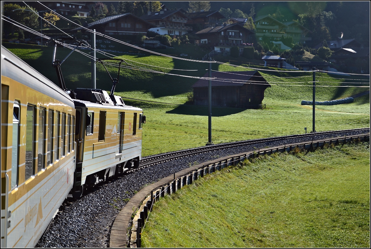 Interessante Fahrt der MOB im Schlepptau von Gepäcktriebwagen GDe 4/4 6005. Bahnstrecke mit Chalets im Hintergrund oberhalb Gstaad. September 2014.