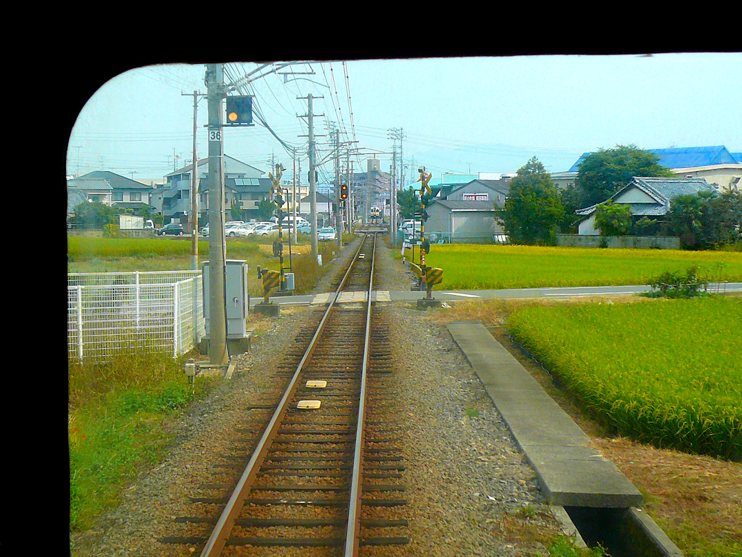 Iyo-Bahn, Gunchû-Linie: Blick auf die bevorstehende Kreuzung mit einem Gegenzug in Okada. Bunt zusammengewürfelte Landschaft mit eher städtischen Bauten, Bauernhäusern und überall kleinen Reisfeldern. 18.September 2009. 