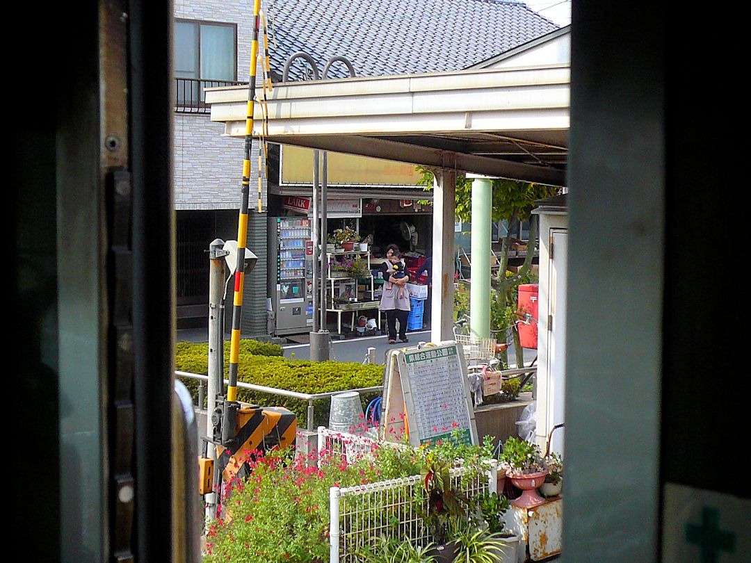 Iyo-Bahn, Gunchû-Linie: Während mein Zug in Jizômachi auf die Kreuzung mit Zug 824 wartet, geht der Blick zur Türe hinaus in die Umgebung des ländlichen Bahnhofs mit seinen Tante-Emma-Läden und wie überall mit Müttern und Kindern. 18.September 2009. 
