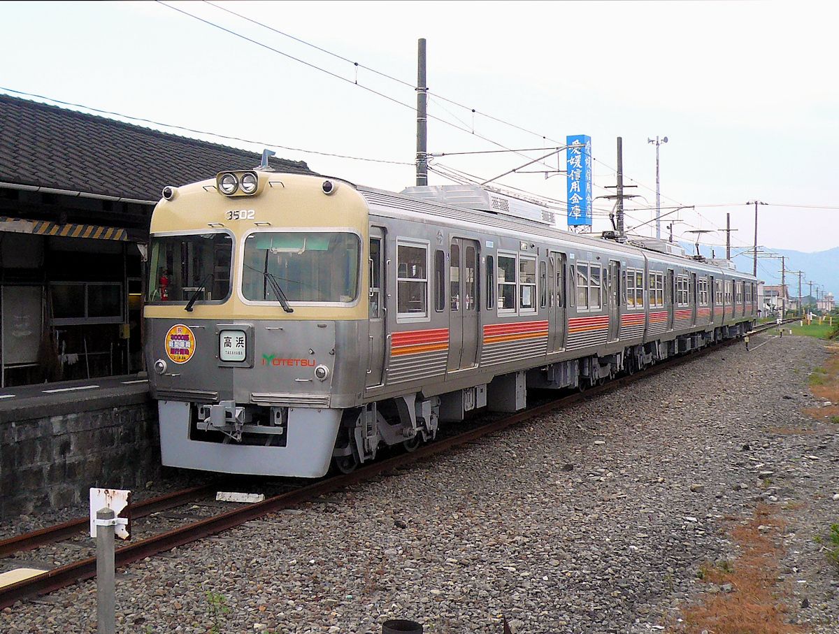 Iyo-Bahn: Iyo ist der alte Provinzname der heutigen Präfektur Ehime im Nordwesten der japanischen Insel Shikoku. Die Iyo-Bahn, die auch Busse betreibt und in der Reise- und Warenhausbranche u.a.m. aktiv ist, besitzt ausser der Strassenbahn von Matsuyama drei Linien, die von Matsuyama ausstrahlen. Ein grosser Teil des Netzes stammt aus den Jahren 1888-1896 und war ursprünglich 762 mm-Spur. Seit 1937 beträgt die Spurweite überall 1067 mm. Die Bahn war wichtig, um die alte Burgstadt Matsuyama mit den Häfen an der Inlandsee (gegenüber Hiroshima) zu verbinden, und um das Hinterland zu erschliessen. Im Bild steht der soeben von der Hektik der Inokashira-Linie des Keiô-Konzerns in Tôkyô auf die beschauliche Insel Shikoku verkaufte Zug 3302-3102-3502 in Yokogawara, 18.September 2009.  