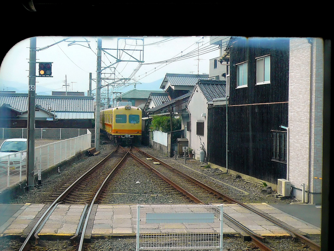 Iyo-Bahn im Nordwesten der Insel Shikoku, Gunchû-Linie von der Stadt Matsuyama aus nach Südwesten: Kreuzung mit dem alten Zug 824, der von der S-Bahn in Tôkyô (Keiô Konzern) stammt. Das charakteristische Schwarz vieler Bauernhäuser stammt daher, dass das Holz zum Schutz gegen die sehr hohe Luftfeuchtigkeit im Sommer leicht angekohlt wird. Jizômachi, 18.September 2009. 