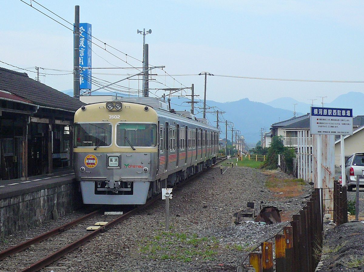 Iyo-Bahn: Yokogawara-Linie (13,2 km lang), Endstation Yokogawara im östlichen Hinterland von Matsuyama, mit Blick auf die hohen Berge von Shikoku. Der aus Tôkyô (Keiô- Konzern, Inokashira Linie) gekommene Neuzugang (Zug 3502) bei der Iyo-Bahn ist erst einige Wochen hier. Zwischen August 2009 und März 2012 kamen 10 Züge Serie 3000 ganz aus rostfreiem Stahl (nach Verkürzung von Fünf- zu Dreiwagenzügen) hierher; Baujahre 1983/84, die letzten 10 Züge einer äusserst erfolgreichen Bauart (ab 1962 gebaut) des Keiô-Konzerns. 18.September 2009. 