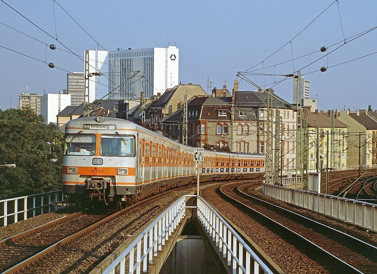 Jahrelang bestimmte die Baureihe 420 das Erscheinungsbild der S-Bahn Rhein-Main. 420 731 erklimmt im Juli 1987 die Rampe zum Hochbahnsteig in Frankfurt West. Aufmerksame Betrachter werden entdecken, dass es den Frankfurter Messeturm, der heute dieses Motiv dominiert, damals noch nicht gab. 