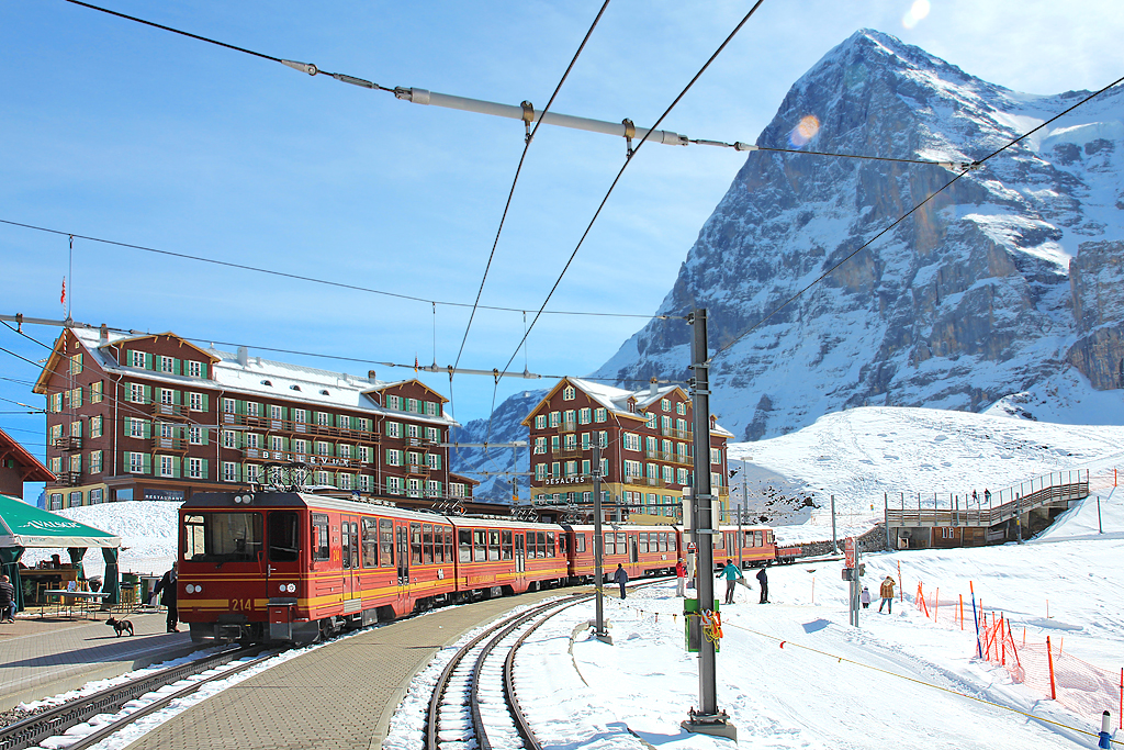 JB-Triebzug BDhe 4/8 Nr. 214 + ? verlässt gerade den Bahnhof Kleine Scheidegg und fährt in Richtung Jungfraujoch. Rechts im Bild erhebt sich der Eiger (3970 m ü. M.). Aufnahme vom 10. April 2016, 11:00