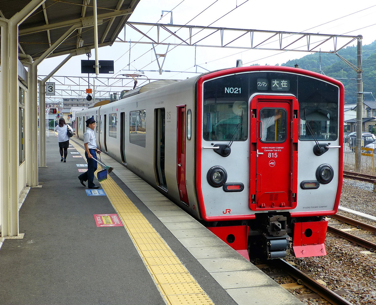 JR Kyûshû Serie 815. Im Jahre 1999 wurden für den elektrischen Betrieb in der Mitte der japanischen Südinsel Kyûshû 26 Zweiwagenzüge (Wechselstrom 20 kV/60 Hz) beschafft. Ein Teil der Züge ist für Lokaldienste um die Stadt Kumamoto an der Westküste stationiert, der andere Teil für Züge um die Stadt Ôita an der Ostküste. Jeder Zug besteht aus einem motorisierten Wagen (KUMOHA 815) und einem unmotorisierten Wagen (KUHA 814). Im Bild steht Zug 815 Nr.21 in Kamegawa an der Ostküste. Der junge Stationsmitarbeiter muss ihn reinigen gehen. 27.Juli 2013 