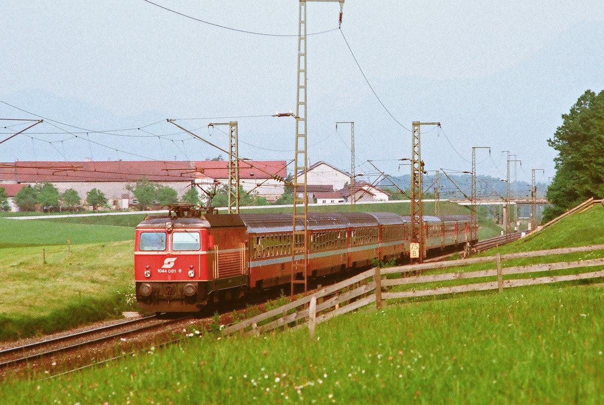 Juli 1988, Wenige Kilometer vor Freilassing fährt ein Zug der ÖBB mit der ÖBB-Lok 1044 081-6 auf der Korridorstrecke bei Straß in Richtung Salzburg. 