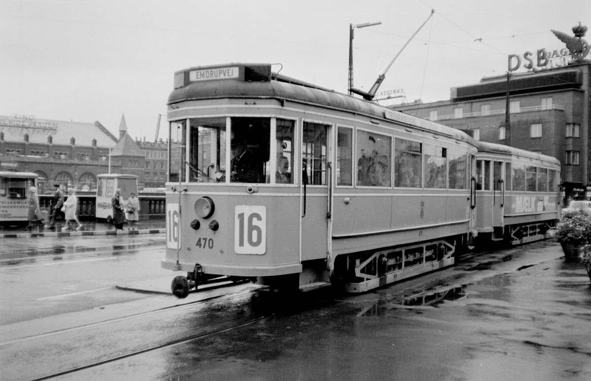 København / Kopenhagen KS: Sonderfahrt / Fotofahrt mit dem Tw 470 und dem Bw 1054 als SL 16. - Der Zug hält in der Vesterbrogade am  Frihedsstøtten  (: am Freiheitsmomument), das rechts außerhalb des Bildes steht. Dieses Monument wurde im Jahre 1791 zur Erinnerung der Aufhebung der Erbuntertänigkeit (1788) errichtet. - Rechts hinter dem Beiwagen lag damals das DSB-Reisebüro  Astoria  (diesen Serviceteil der DSB gibt es nicht mehr!). - Im Hintergrund links sieht man einen Teil des Kopenhagener Hauptbahnhofs, das von Heinrich Wenck, dem Chefarchitekten der Staatsbahnen, am Anfang des 20. Jahrhunderts entworfen wurde. Der Bahnhof wurde am 1. Dezember 1911 geöffnet. - Auf dem Bürgersteig sieht man zwei verschiedene Wägelchen, vom linken verkaufte man  smørrebrød , dh. belegtes Schwarzbrot, vom rechten Eis. - Eine dritte Art Wägelchen gab es in viel größeren Mengen, nämlich die Wurstwagen (man kann noch Wurstwagen finden, aber nicht mehr so viele!). - Scan von einem S/W-Negativ. Film: Ilford FP3. Kamera: Konica EE-matic.