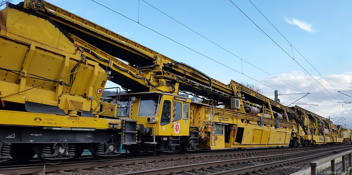 KBS 650 - Zwingenberg nördlich des Bahnhofs am 14.03.2020: Die Spitze der Recycling Planumsverbesserungsmaschine RMPW 2002-2 (99 80 9415 002-1)der Firma Wiebe, in der offensichtlich der Großteil der Energieversorgung stekt. Der Arbeitszug hat die ersten etwa 200 Meter Gleis bearbeitet. Das Planum wird mit diesem Großgerät von Plasser&Theurer in einem Zug gleichzeitig verbessert und der Schotter aufbereitet. 2 Räumketten nehmen im ersten Schritt den Schotter weg und im 2. Schritt ca. 40 cm Planum. Dieses wird dann mit Neumaterial ersetzt und verdichtet bevor geschottert, grob gerichtet und gestopft wird. Die Maschine selbst ist 140 Meter lang, wiegt 560 Tonnen und ist mit 2400 kW ausgestattet. Wenn alles glatt läuft sind 110 Meter Gleis und 800 Kubikmeter Schotter pro Stunde bearbeitet. Weitere Deatils gibt es bei Weibe auf der Homepage.
P.S. Das Bild habe ich jetzt aufgerichtet