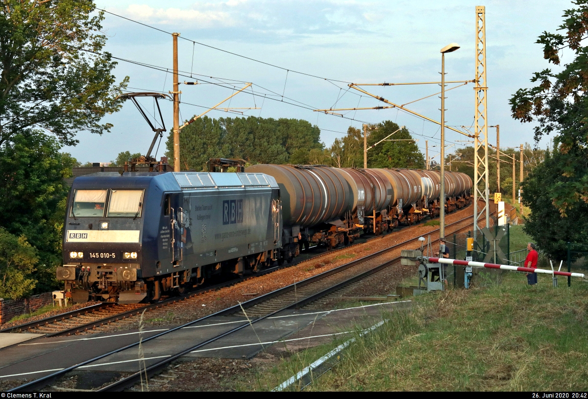 Kesselzug mit 145 010-5 (Lok 210) DB, vermietet an die RBH Logistics GmbH, passiert die Anrufschranke in Zscherben, Angersdorfer Straße, auf der Bahnstrecke Halle–Hann. Münden (KBS 590) Richtung Teutschenthal.
[26.6.2020 | 20:42 Uhr]