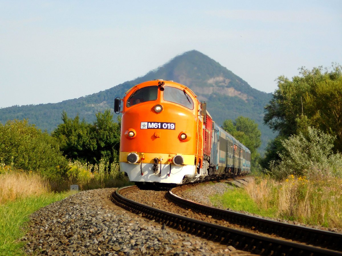 Klassisches Motiv von der Strecke Balaton Nordufer: Die M61 019 und M62 001 mit dem Zug 19704 kurz vor Tapolca. Der Berg hinter den Lokomotiven ist der vulkanischer Zeugenhügel  Gulács 
Das Bild ist von meines Sohn Márk Németh.
Tapolca, 02.08.2020.
