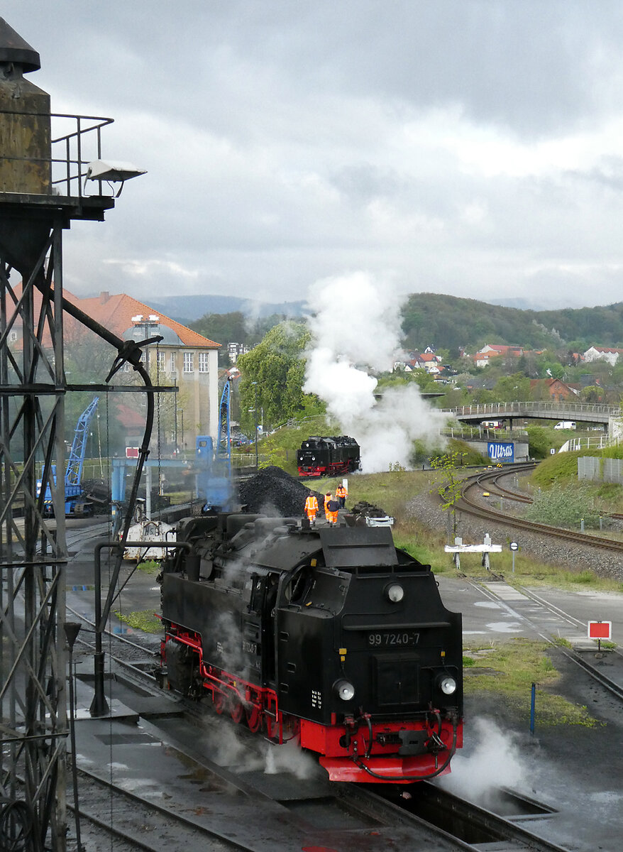 Kleine, orange Männchen auf der Dampflok? Nein, das gut sichtbare Personal ist auf dem Depotgelände unterwegs. Während die Lok im Vordergrund zum Belad mit Kohle unterwegs ist, rollt jene im Hintergrund in den Personenbahnhof und fährt an die bereit stehenden Wagen an. Das Ganze ist sehr gut von der Aussichtsplattform beim Bahnhof Wernigerode zu verfolgen. Wernigerode, 17.4.2024