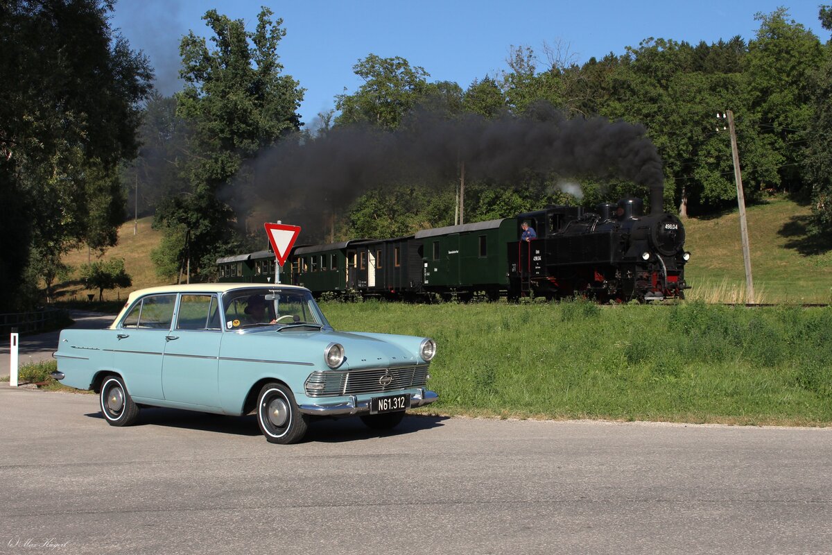 Knapp 30 Jahre Altersunterschied liegen zwischen dem blauen Opel Rekord und der 498.04 die hier kurz vor dem Bahnhof Sommerhuberm�hle am 25.7.2026 mit ihrem Personenzug von Steyr Lokalbahnhof nach Gr�nburg f�hrt.