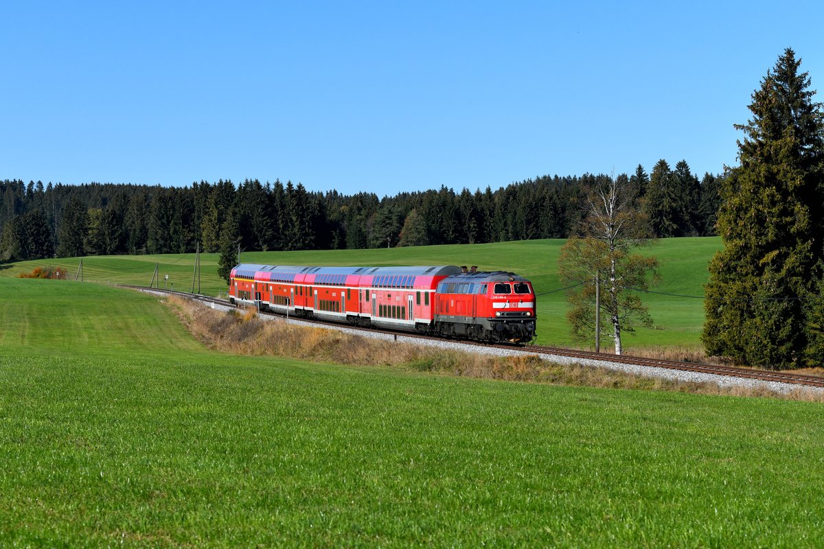 Kurz vor dem Bahnhof Weizern-Hopferau konnte ich am 14. Oktober 2018 die RB 57370, geführt von 218 496, bei Eisenberg fotografieren. Lok und Wagen bildeten an diesem Tage die Garnitur für den damals am Wochenende zusätzlich verkehrenden Neuschwanstein-Express. Das Stilllager in Füssen wurde stets dafür genutzt, den Zug als Regionalbahn einmal nach Augsburg und zurück pendeln zu lassen. Erfreulich für Eisenbahnfreunde, denn so hatte man immer eine zusätzliche 218er Leistung, die man ablichten konnte. Die Zuglok 218 496 ist inzwischen auch praktisch Geschichte, nach Übergang des Verkehrs auf die BRB wurde sie aufgrund Fristablaufs am 06.12.2018 z-gestellt. Inzwischen hat sie ihren Motor an eine andere 218 abtreten müssen. 