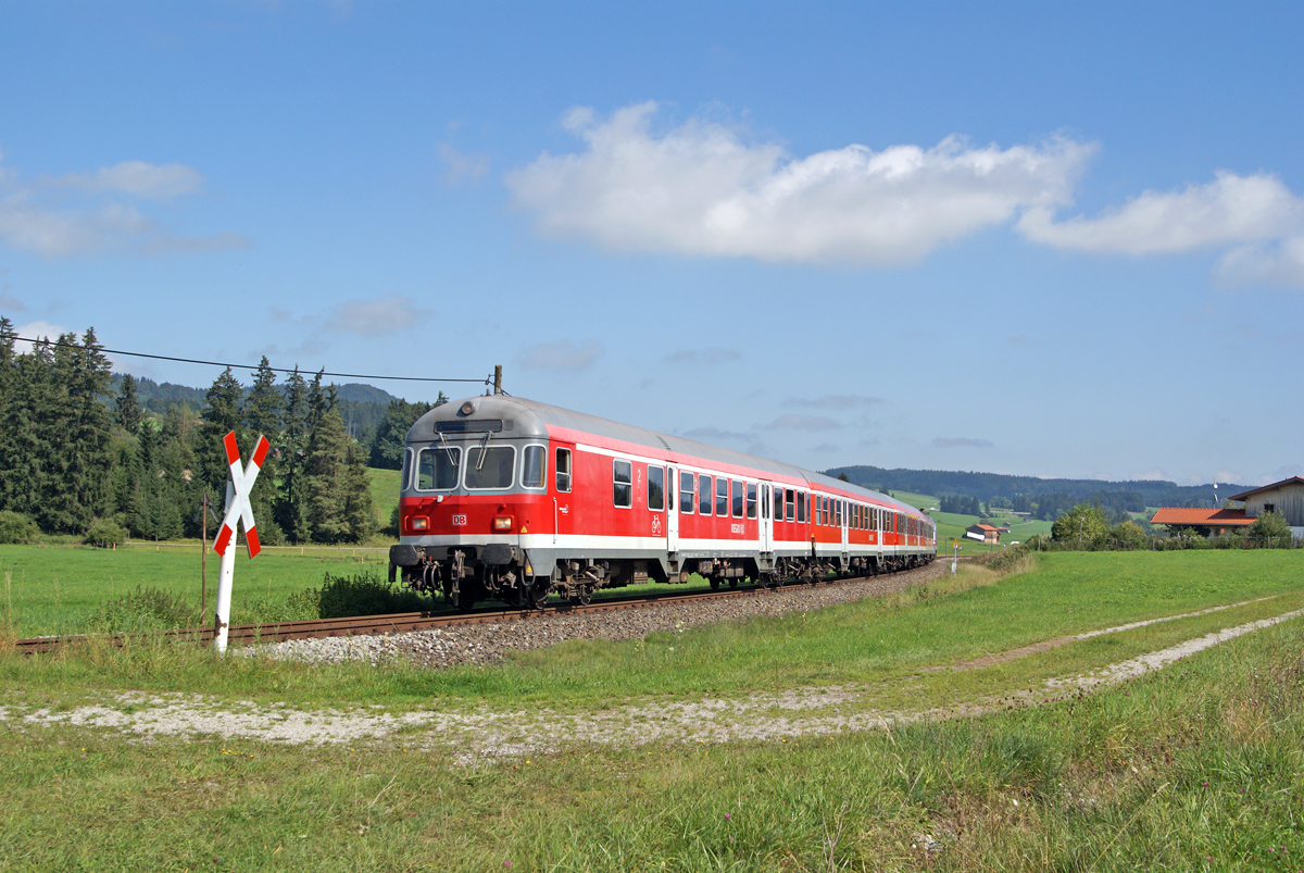Kurz vor Erreichen des Bahnhofes Weizern-Hopferau passiert eine von 218 467 geschobene RB aus Füssen am 15.09.2014 einen technisch nicht gesicherten Bahnübergang.